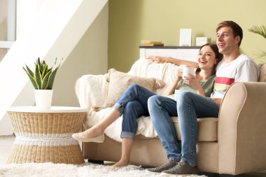 Evde kanepede dinlenirken kahve içen genç çift