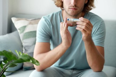 Diyabetli adam evde tükenmez kalemle kan örneği alıyor.