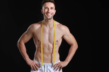 Koyu arkaplanda mezurası olan yakışıklı kaslı adam. Kilo verme konsepti