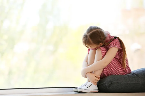 Niña triste con trastorno autista sentada en el alféizar de la ventana en casa —  Fotos de Stock