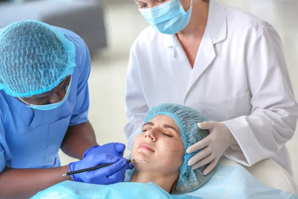 Klinikte ameliyat öncesi kadının yüzüne işaret uygulayan plastik cerrah — Stok fotoğraf