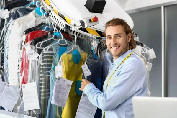 Worker of modern dry-cleaner\'s near rack with clothes