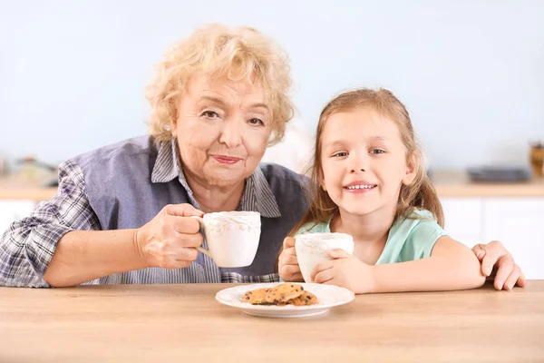 Linda niña y abuela bebiendo té con galletas en la cocina —  Fotos de Stock