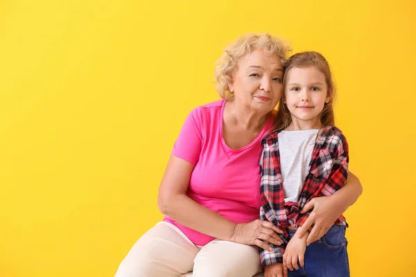 Cute little girl with grandmother on color background — Stock Photo, Image
