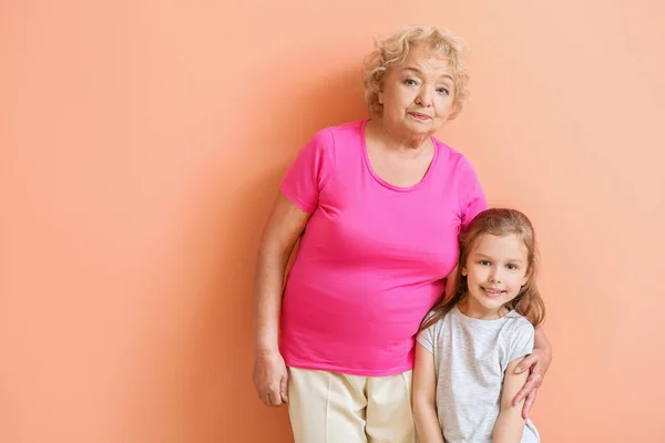 Cute little girl with grandmother on color background — Stock Photo, Image