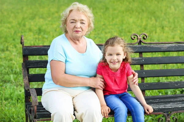 Милая маленькая девочка с бабушкой, сидящей на скамейке в парке — стоковое фото