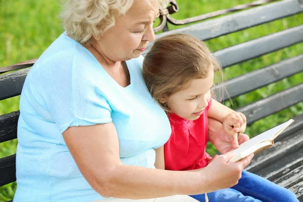Χαριτωμένο κορίτσι διαβάζει το βιβλίο με τη γιαγιά στο πάρκο — Φωτογραφία Αρχείου