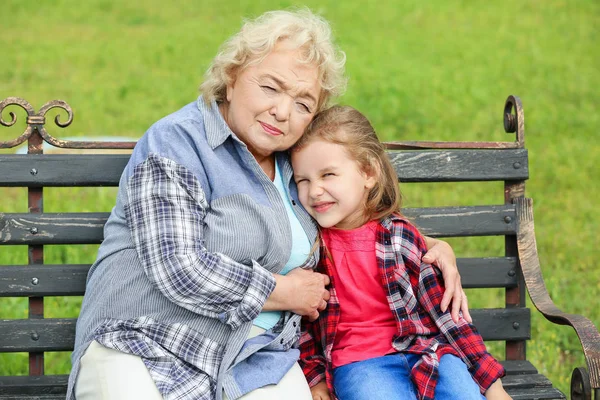 Menina bonito com a avó sentada no banco no parque — Fotografia de Stock