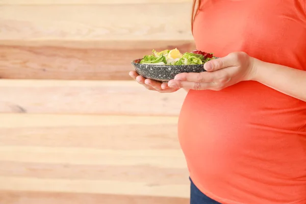 Beautiful pregnant woman with healthy salad on wooden background — Stock Photo, Image