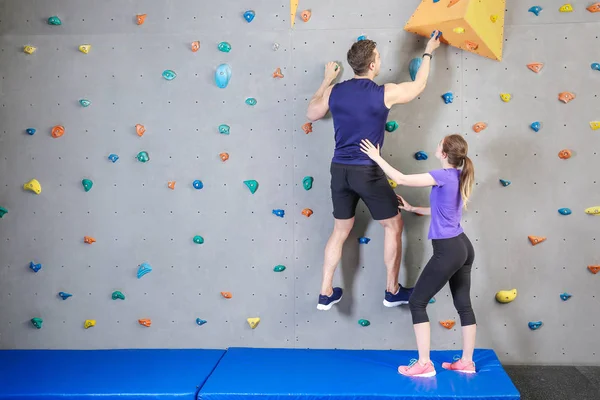 Инструктор учит молодого человека лазить по стене в спортзале — стоковое фото