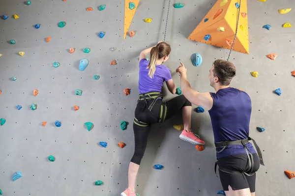 Instructor enseñando a la joven a escalar la pared en el gimnasio — Foto de Stock