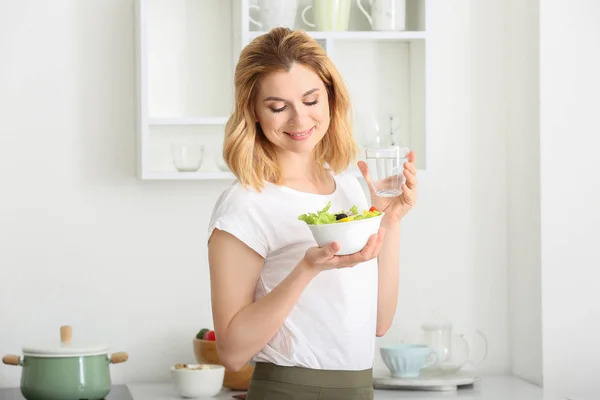 Mulher com salada de legumes saudável e copo de água na cozinha — Fotografia de Stock