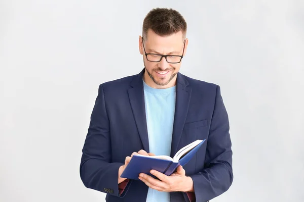 Schöner männlicher Lehrer mit Buch auf hellem Hintergrund — Stockfoto