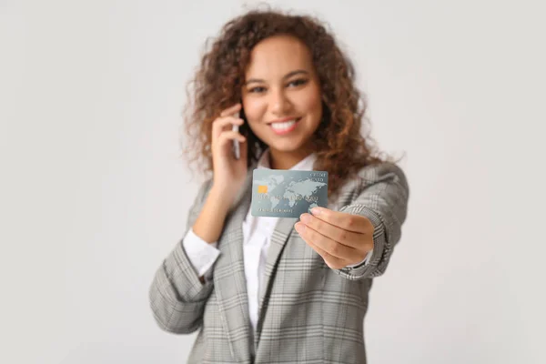 Jeune femme d'affaires afro-américaine avec carte de crédit parlant par téléphone sur fond clair — Photo