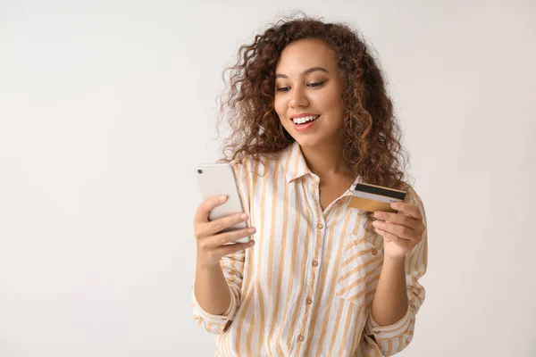 Belle femme afro-américaine avec carte de crédit et téléphone portable sur fond clair — Photo