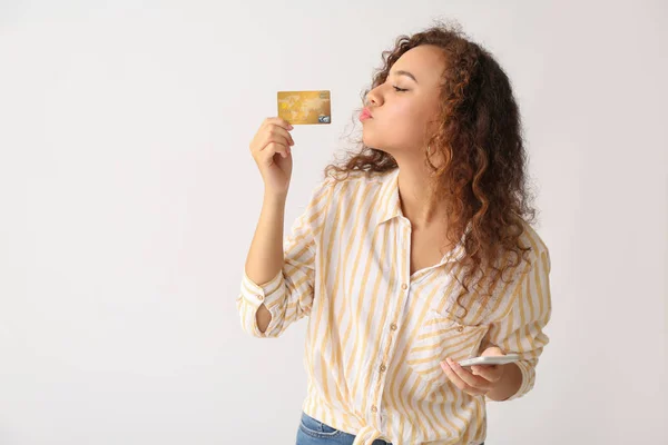 Hermosa mujer afroamericana con tarjeta de crédito y teléfono móvil sobre fondo claro — Foto de Stock