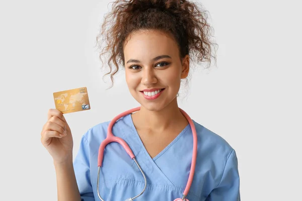 Médico afro-americano com cartão de crédito em fundo claro — Fotografia de Stock