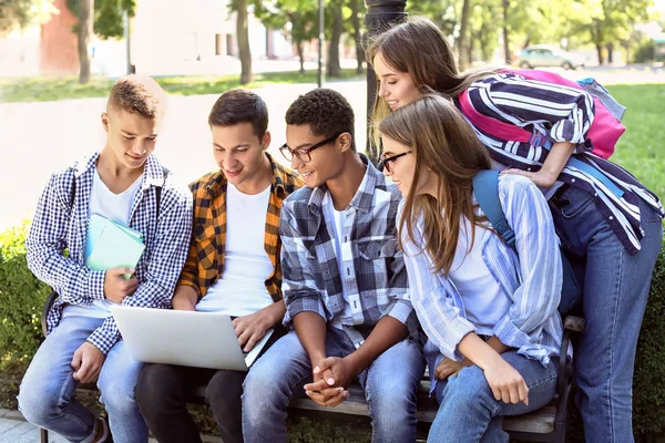 Молоді студенти з ноутбуком сидять на лавці на відкритому повітрі — стокове фото
