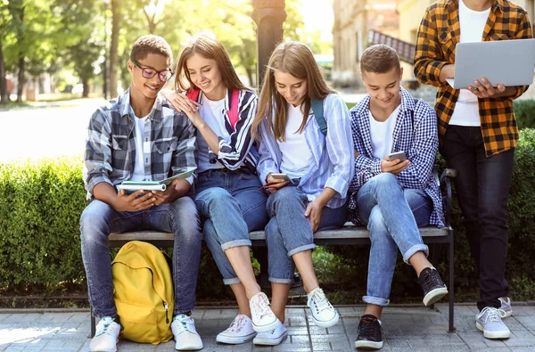 Jonge studenten zitten op de Bank buitenshuis — Stockfoto