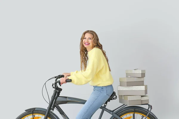 Mulher bonita com caixas de presente e bicicleta no fundo claro — Fotografia de Stock