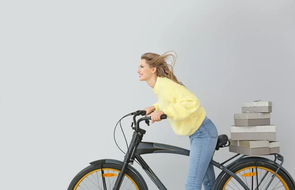 Beautiful young woman with gift boxes and bicycle on light background — Stock Photo, Image