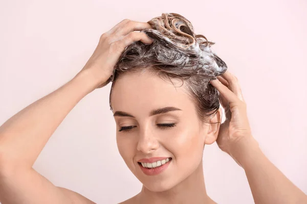 Beautiful young woman washing hair against light color background