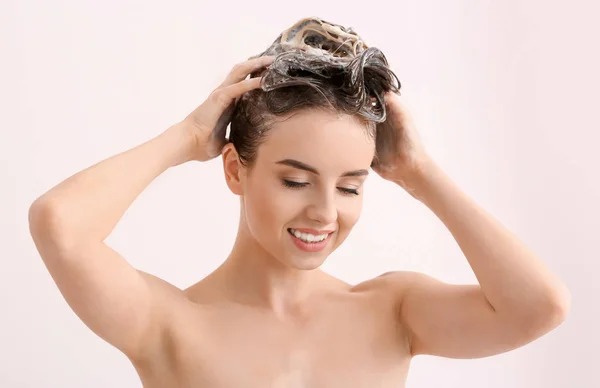 Красива молода жінка миє волосся на фоні світлого кольору — стокове фото