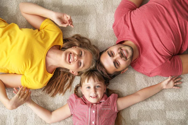 Portrait of happy young family lying on carpet at home — Stock Photo, Image