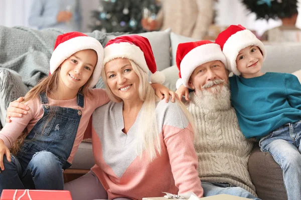 Glückliche Großeltern und kleine Kinder in Weihnachtsmannhüten zu Hause — Stockfoto