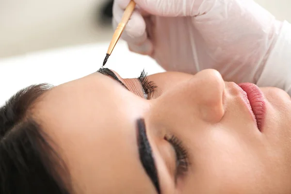 Young woman undergoing eyebrow correction procedure in beauty salon, closeup