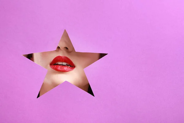 Lippen van mooie jonge vrouw zichtbaar door ster knippen in kleur papier — Stockfoto