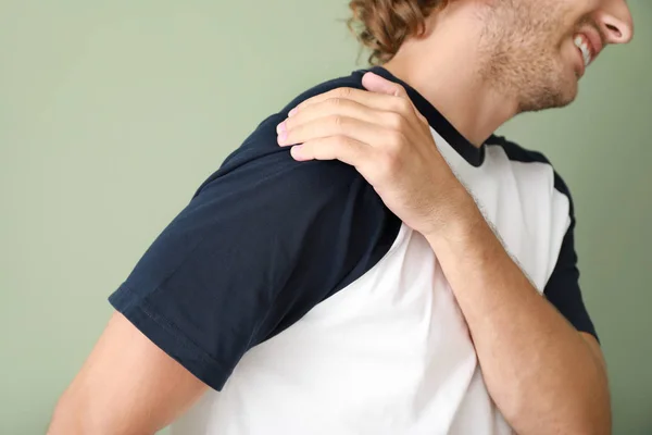 Mladý muž trpící bolestí v rameni na barevném pozadí — Stock fotografie