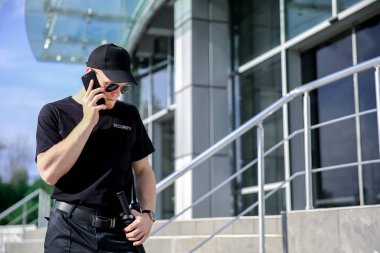 Yakışıklı erkek güvenlik görevlisi telefonla açık havada konuşuyor