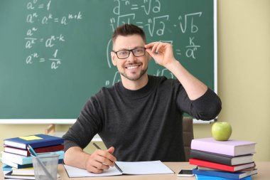 Yakışıklı matematik öğretmeni sınıfta masada oturuyor