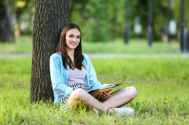 Güzel kadın öğrenci parkta ağaç altında oturuyor
