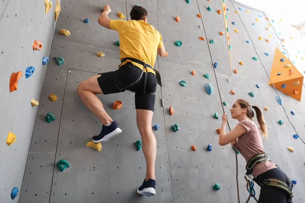 Jovem com instrutor parede de escalada no ginásio — Fotografia de Stock
