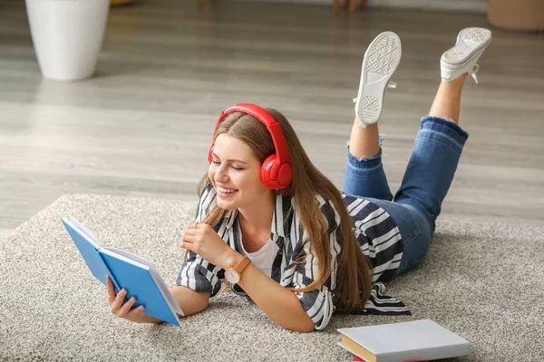 Genç kadın evde müzik dinleme ve kitap okuma — Stok fotoğraf