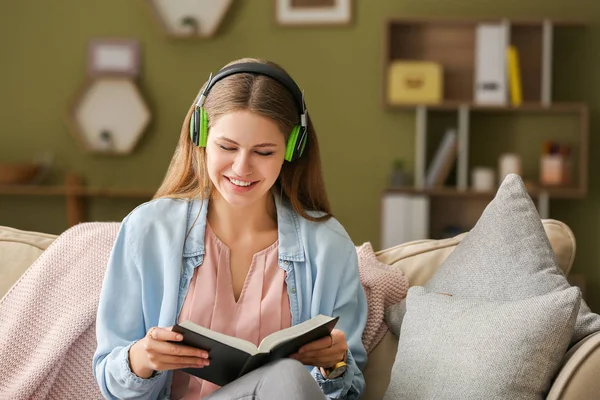 Νέα γυναίκα ακούγοντας μουσική και διαβάζοντας το βιβλίο στο σπίτι — Φωτογραφία Αρχείου