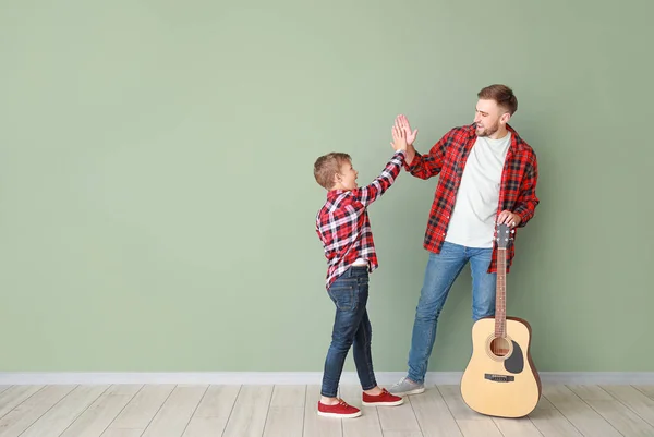 Feliz padre e hijo con la guitarra dando uno al otro chocan cinco cerca de la pared de color — Foto de Stock