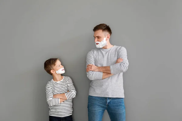 Father and his little son with shaving foam on faces against grey background — Stock Photo, Image