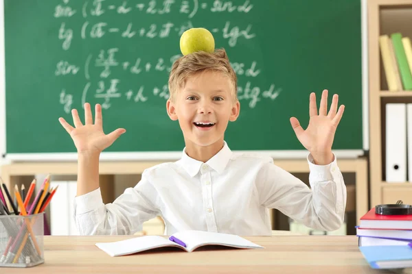 Kleiner Junge mit Apfel sitzt am Schreibtisch im Klassenzimmer — Stockfoto