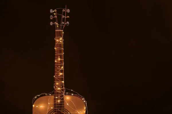 Guitarra com guirlanda de Natal brilhante no fundo escuro — Fotografia de Stock