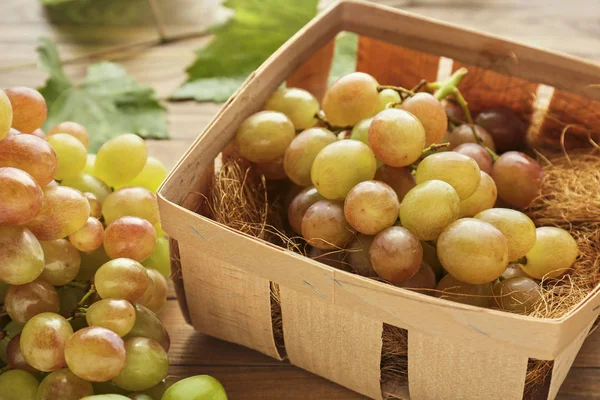 Basket with tasty sweet grapes on wooden table — Stock Photo, Image
