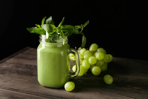 Mason jar of tasty smoothie with ingredients on table against dark background — Stock Photo, Image