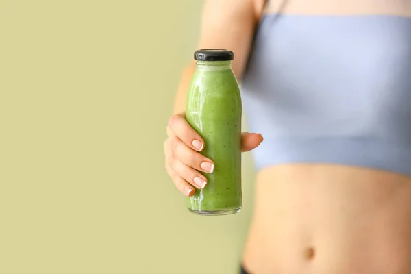 Sporty woman with bottle of tasty green smoothie on color background — Stock Photo, Image