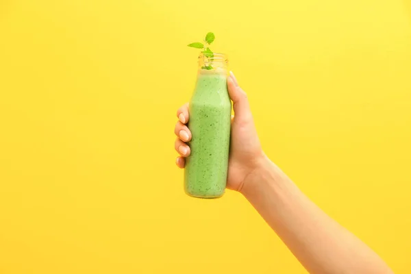 Mão feminina com saboroso smoothie verde em garrafa sobre fundo de cor — Fotografia de Stock