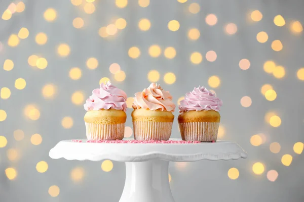 Cupcakes de aniversário saborosos em pé contra luzes desfocadas — Fotografia de Stock