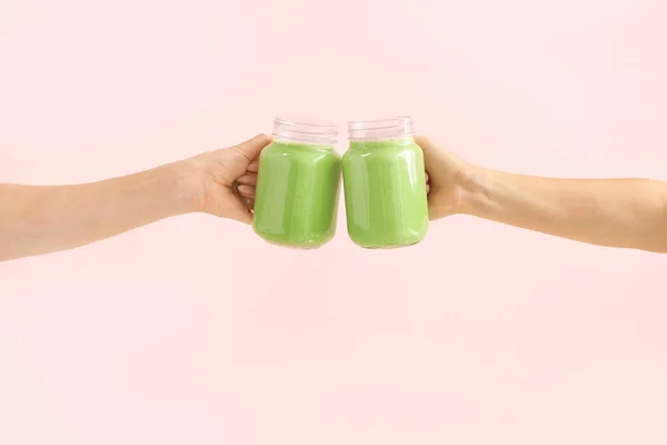 Mãos femininas com saboroso smoothie verde em frascos de pedreiro no fundo de cor — Fotografia de Stock