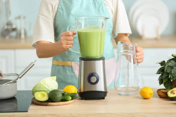 Young woman making tasty green smoothie in kitchen at home — Stock Photo, Image