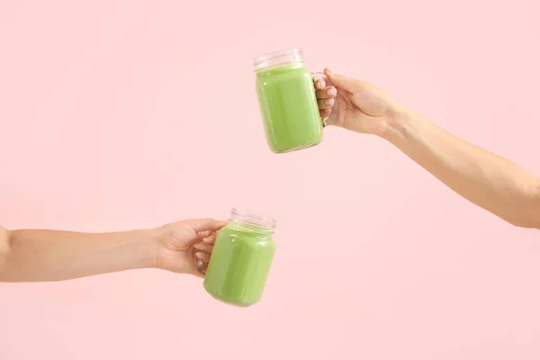 Mãos femininas com saboroso smoothie verde em frascos de pedreiro no fundo de cor — Fotografia de Stock